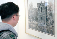 Martin Truong, freshman undecided major, examines a painting by Jim Bray, professor of art. The piece is one of 38 in an exhibit at Spiva Art Gallery honoring Bray before his retirement in June. This painting tells the story of when BrayÂ´s family moved to Oklahoma.
