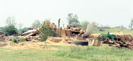 An individual surveys tornado damage done to a house.
