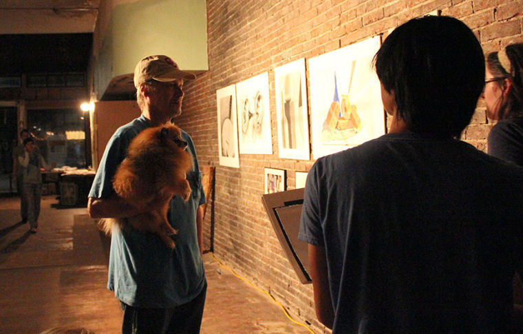 Holding Hershey the Pomeranian, Richard Henning, left, of Carl Junction, talks with students as he views the art on display in the Focal Point art gallery in downtown Joplin, Sept. 19. Henning, father of Jade, a senior studio art major, said, “We are very proud of her.” Jade Henning’s design is featured as the print of the month for the September Third Thursday art walk exhibition.