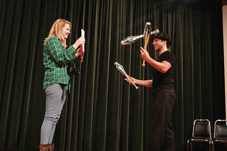 Niamh Quinn a junior mass communications major, holds up a book for comedy juggler Nick Pike to read as he juggles three pins during his performance in Corley Auditorium on Tuesday, April 1, 2014.