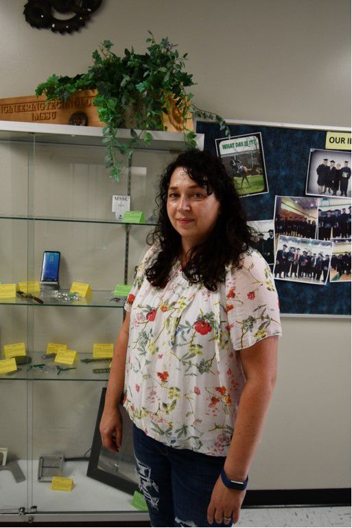 Claudia Wilson, assistant professor, who teaches CNC Project Design & Analysis stands next to a display case containing previous student work. 